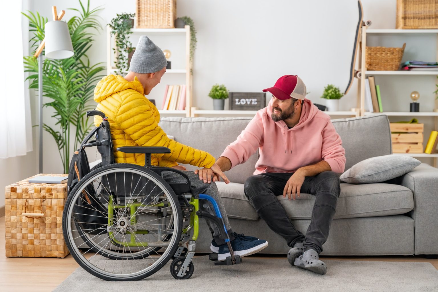 Man supporting a disabled friend in wheelchair at home