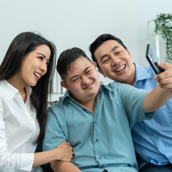 Asian parents and son with autism using phone take a selfies at home.